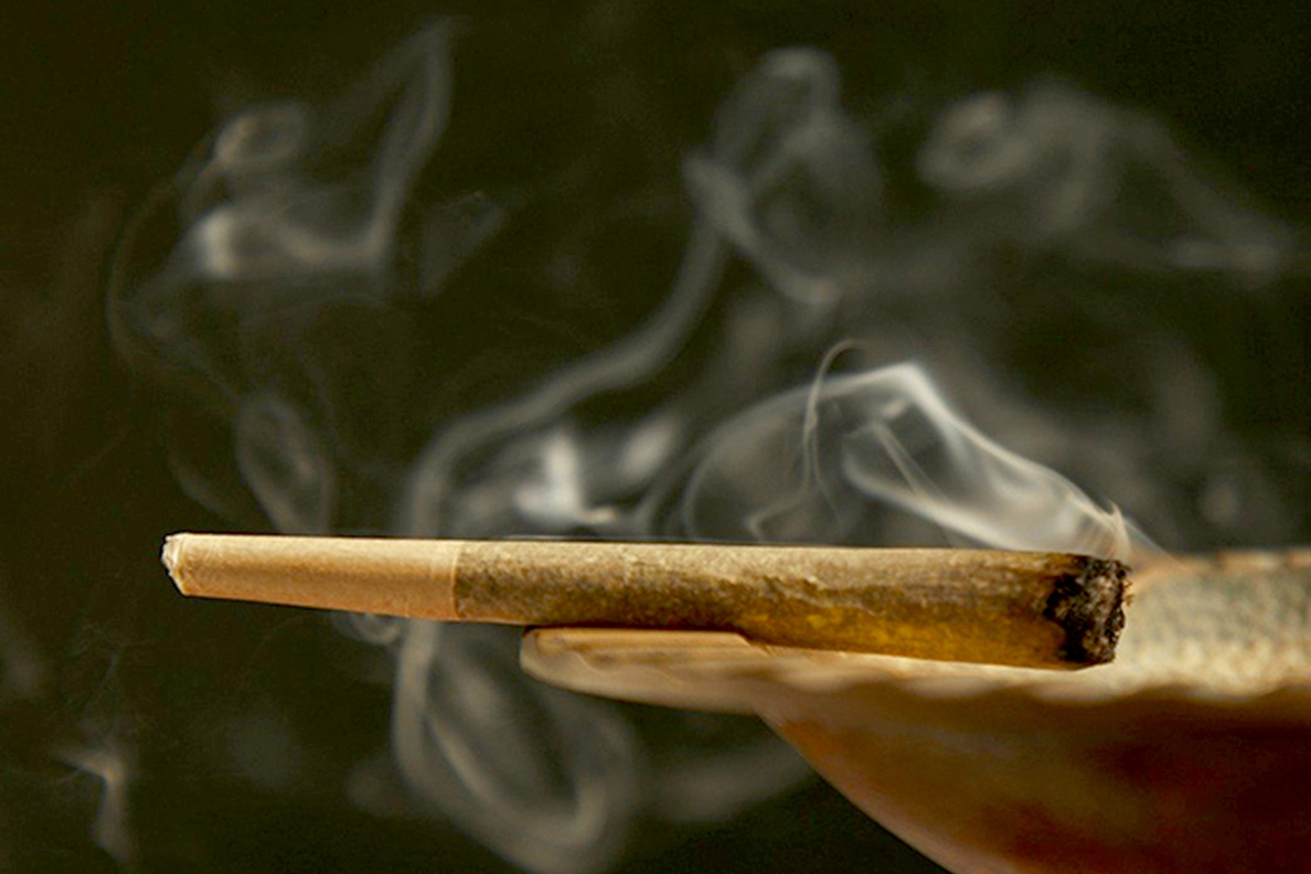 Burning cannabis joint sitting on the edge of a dish.